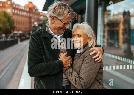 Affectionate senior man embracing woman while waiting at bus stop Stock Photo