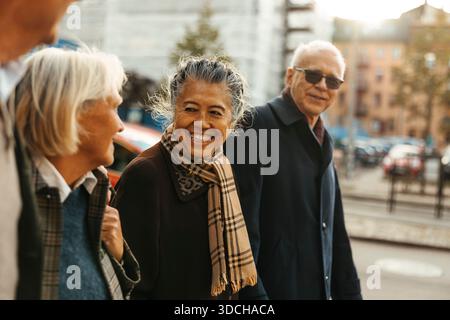Smiling elderly woman walking with friends while spending leisure time at street Stock Photo