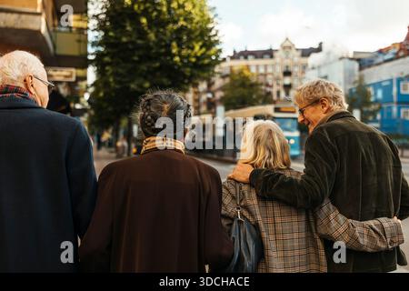 Rear view of male and female senior friends walking side by side at city street Stock Photo