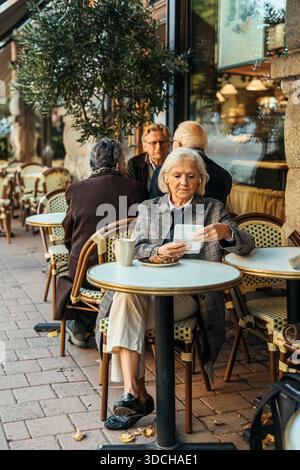 Senior woman using tablet PC while sitting at table in sidewalk cafe Stock Photo