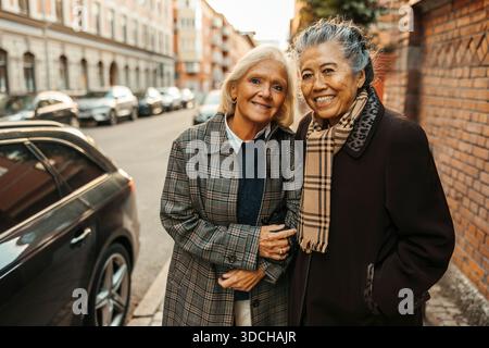 Portrait of smiling elderly woman standing with female friend on sidewalk Stock Photo