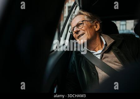 Curious smiling senior man looking out through window while traveling in car Stock Photo