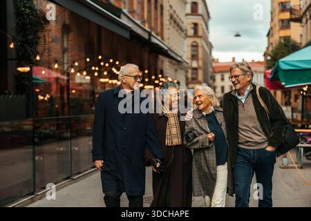 Happy elderly male and female friends talking with each other while walking at city street Stock Photo
