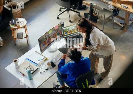 High angle view of female tech professional talking with male colleague working on desktop PC in startup office Stock Photo