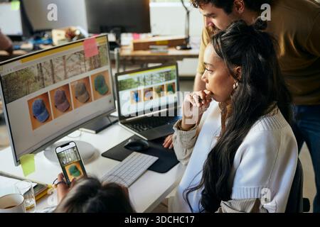 Focused female programmer working with colleagues on desktop PC in startup office Stock Photo
