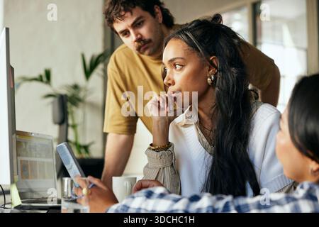 Concentrated female programmer working with colleagues on desktop PC in startup office Stock Photo