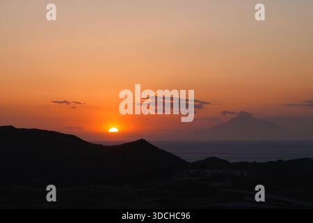 Golden hour sun setting behind dark hills, sea, and distant mount athos Stock Photo