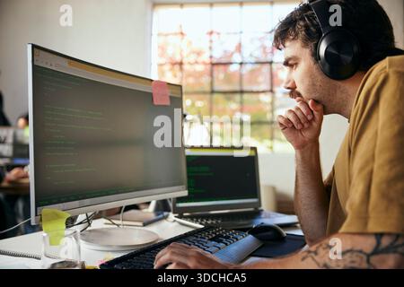 Focused male programmer wearing wireless headphones coding on computer in startup office Stock Photo