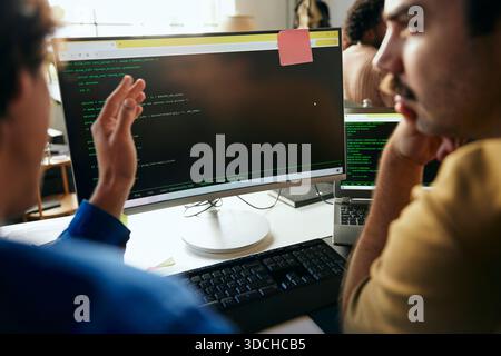 Male programmers discussing ideas with each other while coding on desktop PC in office Stock Photo