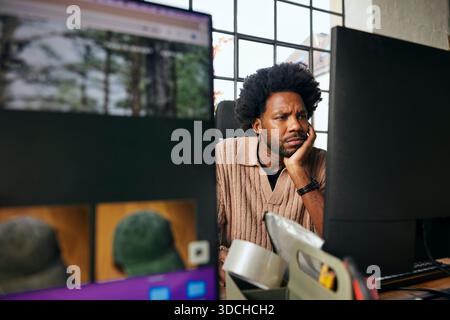 Focused curly haired male tech professional leaning on elbow while working in startup office Stock Photo