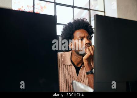 Curly haired male tech professional leaning on elbow while working in startup office Stock Photo