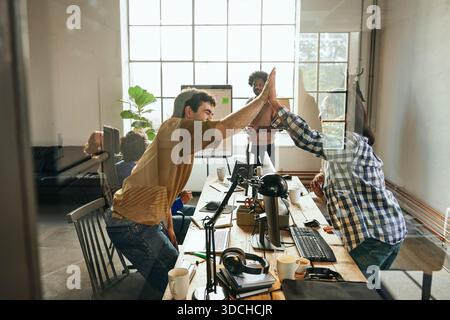 Happy male and female giving high-five to each other in office seen from glass Stock Photo