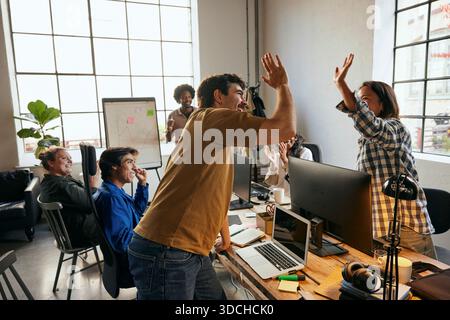 Happy male business expert giving high-five to female colleague while standing near desk in office Stock Photo