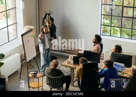 High angle view of female business expert explaining ideas on whiteboard to team in meeting at new office Stock Photo