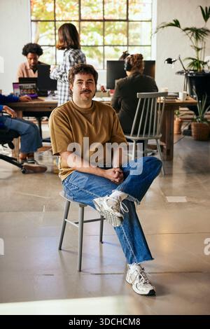 Portrait of confident male business professional sitting on chair in startup office Stock Photo