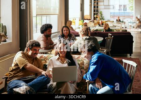 Smiling female business expert using laptop while sitting with male colleagues in tech office lobby Stock Photo