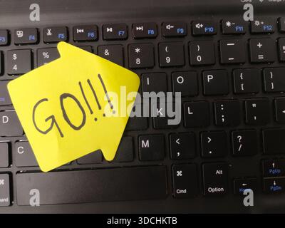 The image shows a yellow, arrow-shaped sticky note with the word GO!!! written on it, placed over a black computer keyboard. Stock Photo
