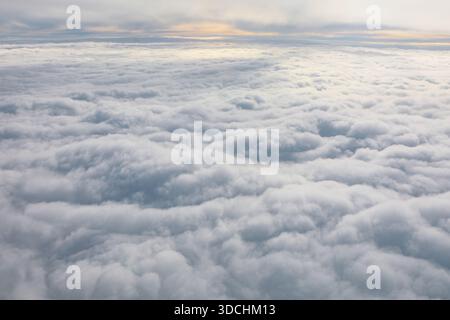 Blanket of clouds stretches endlessly beneath a soft sunrise glow, viewed from high above. Scene feels serene and infinite, with gentle light casting Stock Photo