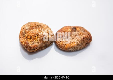 Two preserved, dense dried figs dusted with fine sugar or spice, positioned on white surface. Granular on surface of naturally preserved figs Stock Photo