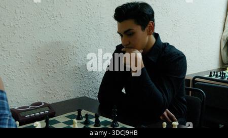 Focused young man leaning on his hand while thinking over chess board. Stock Photo