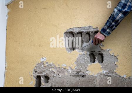 Person repairing a damaged wall with a tool, showing exposed bricks. Stock Photo