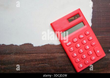 A red calculator placed on torn white paper atop a dark wooden surface. Stock Photo