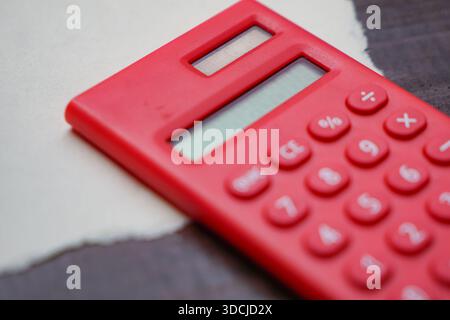 A red calculator placed on torn white paper atop a dark wooden surface. Stock Photo