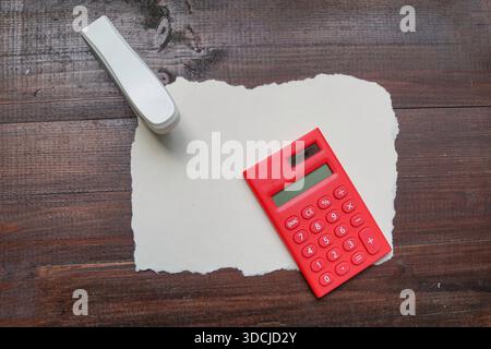 A red calculator and white stapler placed on torn white paper atop a dark wooden surface. Stock Photo