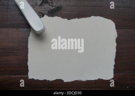 A white stapler placed on torn white paper atop a dark wooden surface. Stock Photo