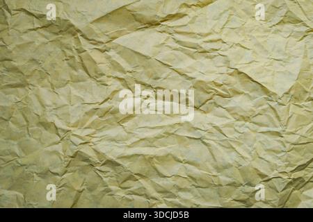 A piece of crumpled yellowish paper with deep folds and wrinkles, creating a distressed and textured appearance. Stock Photo