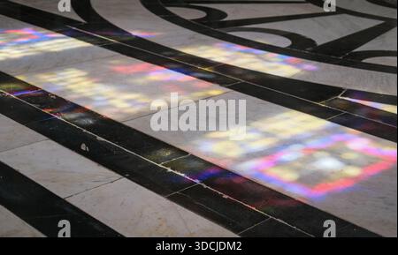 Interior floor detail showing multicolored light reflections from stained glass, black and white marble tiles, polished stone surface Stock Photo