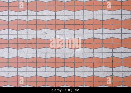 Top-down view of a vintage geometric mosaic tile floor featuring repeating zigzag patterns in muted orange and white tones. Stock Photo