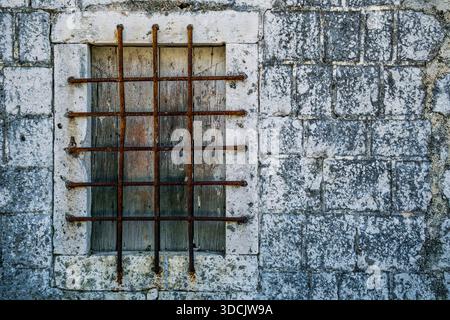 A weathered stone wall with a barred window. Stock Photo