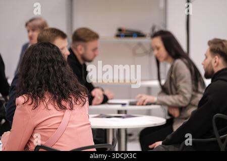 Coworkers sit around round table in bright workspace. They review papers and devices while focused on discussion. Friendly collaborative atmosphere fosters teamwork and planning for upcoming project. Stock Photo