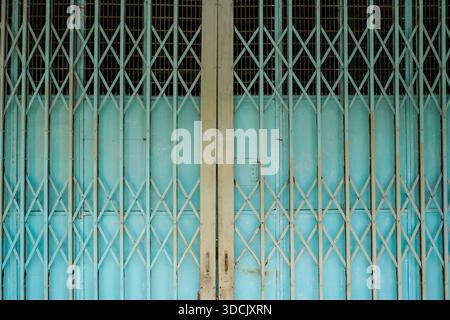 Symmetrical turquoise folding metal gate with diagonal lattice design on a historic shopfront in Malaysia. Stock Photo