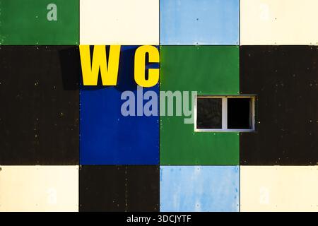 View of a geometric facade with squares of blue, green, black, and white, punctuated by a small window and the bold yellow letters 'WC', Aktau, Mangys Stock Photo