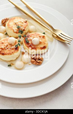 White plate with cottage cheese pancakes, syrniki, curd fritters served with pear balls, walnut and honey on light background, top view Stock Photo