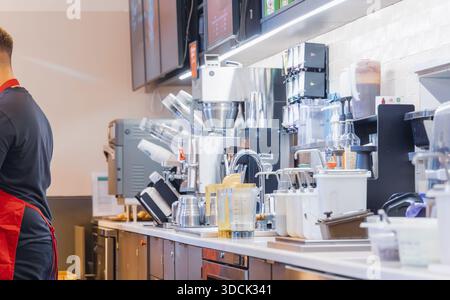 Two cafe workers in uniform preparing drinks at a busy commercial coffee station with espresso machines and equipment Stock Photo