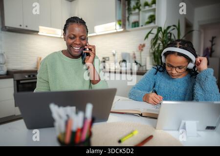 Mother multitasking working from home while daughter remote learning Stock Photo