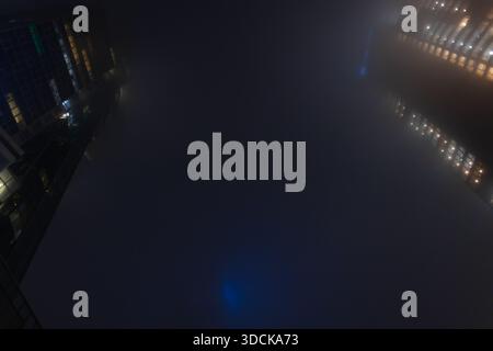 Abstract urban photography of light patterns from building windows blurred by heavy nighttime haze. Foggy night cityscape with illuminated office buil Stock Photo