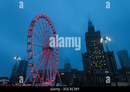Dramatic low-angle view of an illuminated Ferris wheel in Warsaw at twilight. The glowing red attraction stands against a misty blue sky with the icon Stock Photo