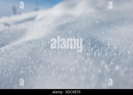 Detailed macro view of untouched snow glistening under bright daylight. The frosty surface reveals natural patterns and subtle contours shaped by wind Stock Photo