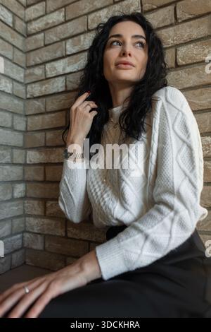 Elegant young female model sitting outside in the sun, dressed in autumn attire, enjoying the warmth of a peaceful afternoon. Stock Photo