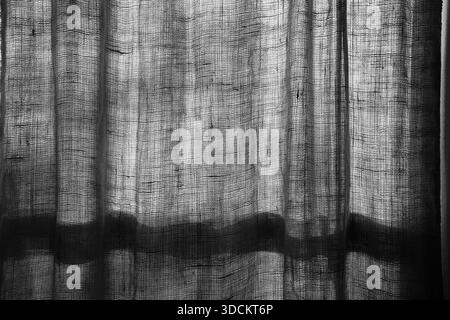 black and white image of light shining through a window curtain with lines and shadows showing on the fabric of the window covering horizontal image w Stock Photo