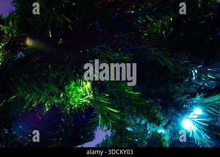 Close-up of green and blue Christmas lights glowing through synthetic pine branches Stock Photo