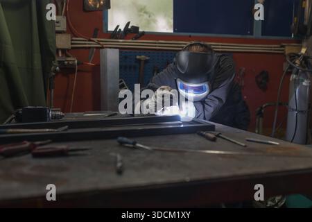 Welder operator wearing personal protective equipment working in the welding workshop, fusing steel parts together, using MIG welding proccess. Metal Stock Photo