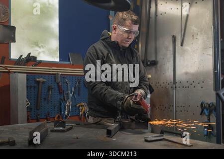 Skillful craftsman using a portable angle grinder in a home workshop, grinding metal while sparkles fly around him. Stock Photo