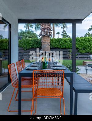 outdoor metal picnic table set for dining party orange chairs on backyard patio end view Stock Photo