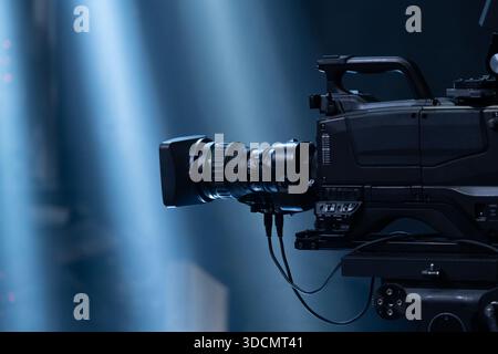 Professional broadcast camera capturing a live concert or event, recording the action with theatrical stage lighting creating dynamic light beams Stock Photo
