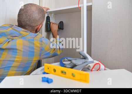 Man installing new shelf with screwdriver, performing home improvement work Stock Photo